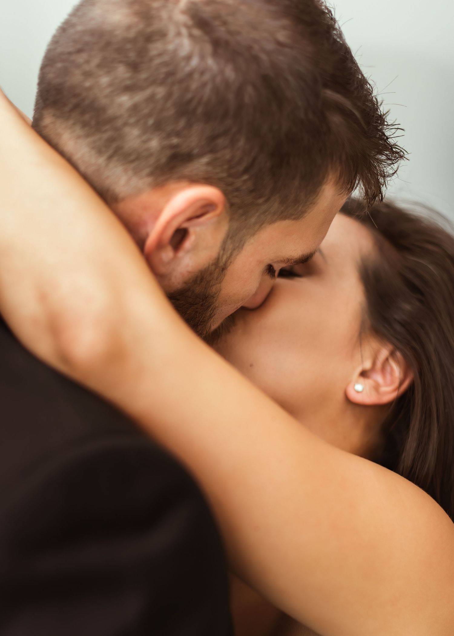 An intimate close-up wedding photo capturing a tender embrace against a light background.