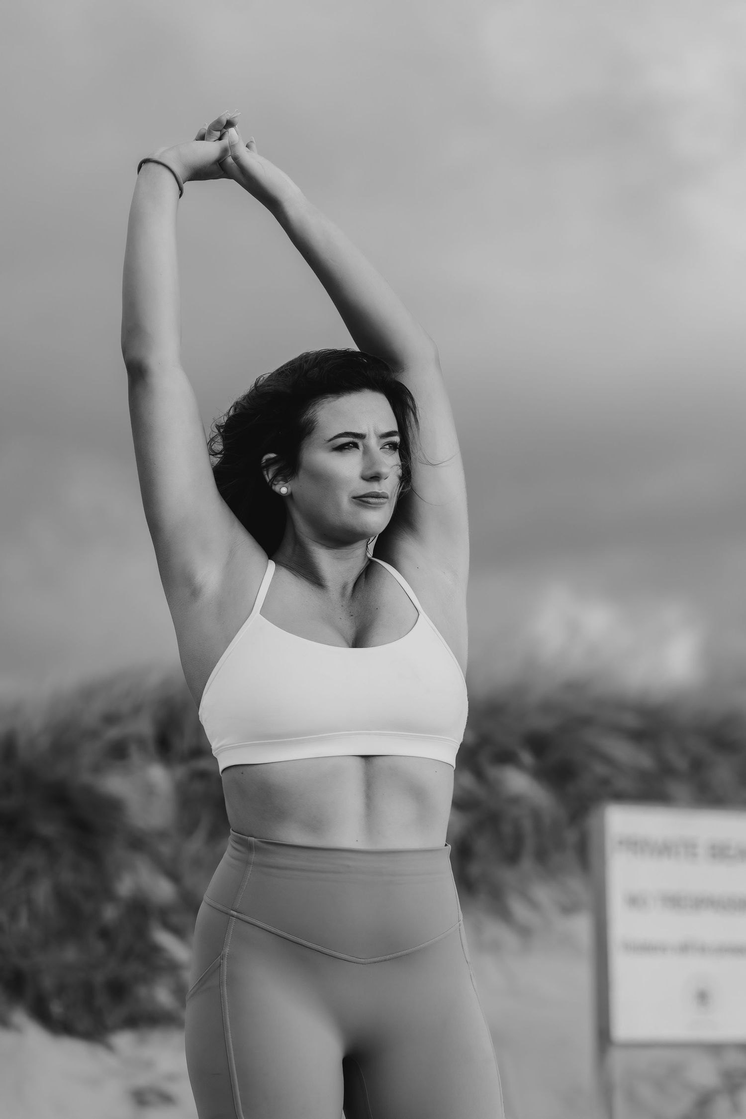 A black and white photo of a woman stretching in workout attire on a beach.