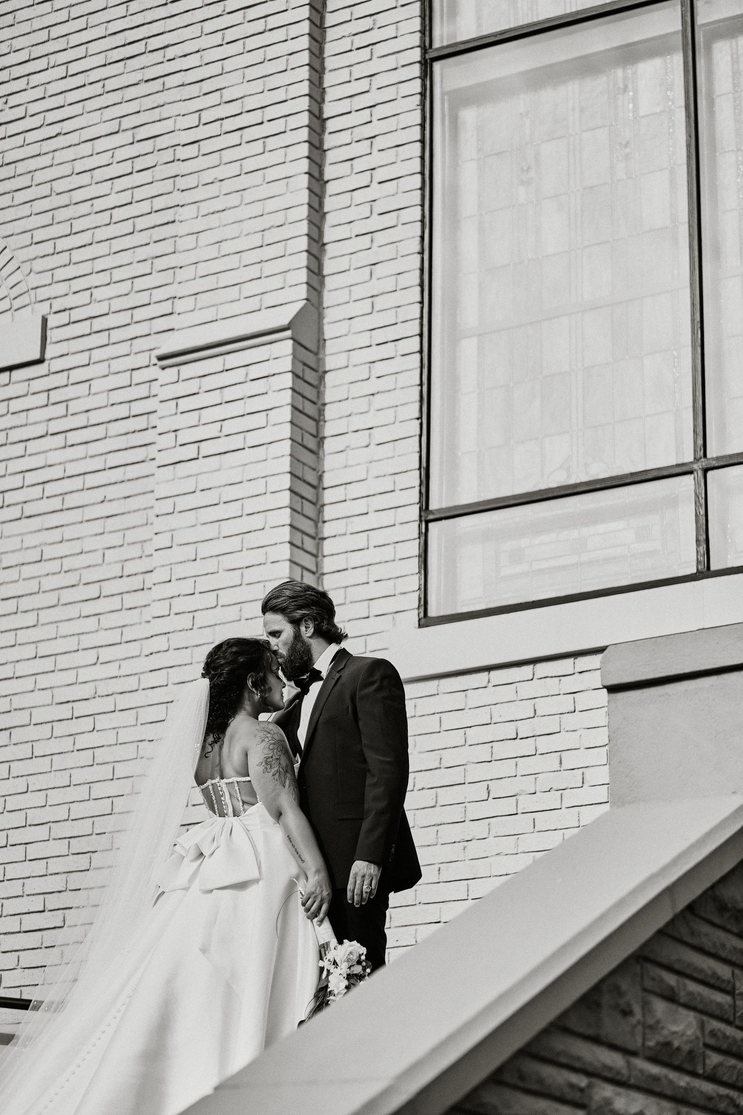 A romantic black and white moment captured of a couple on their wedding day against a brick wall backdrop.