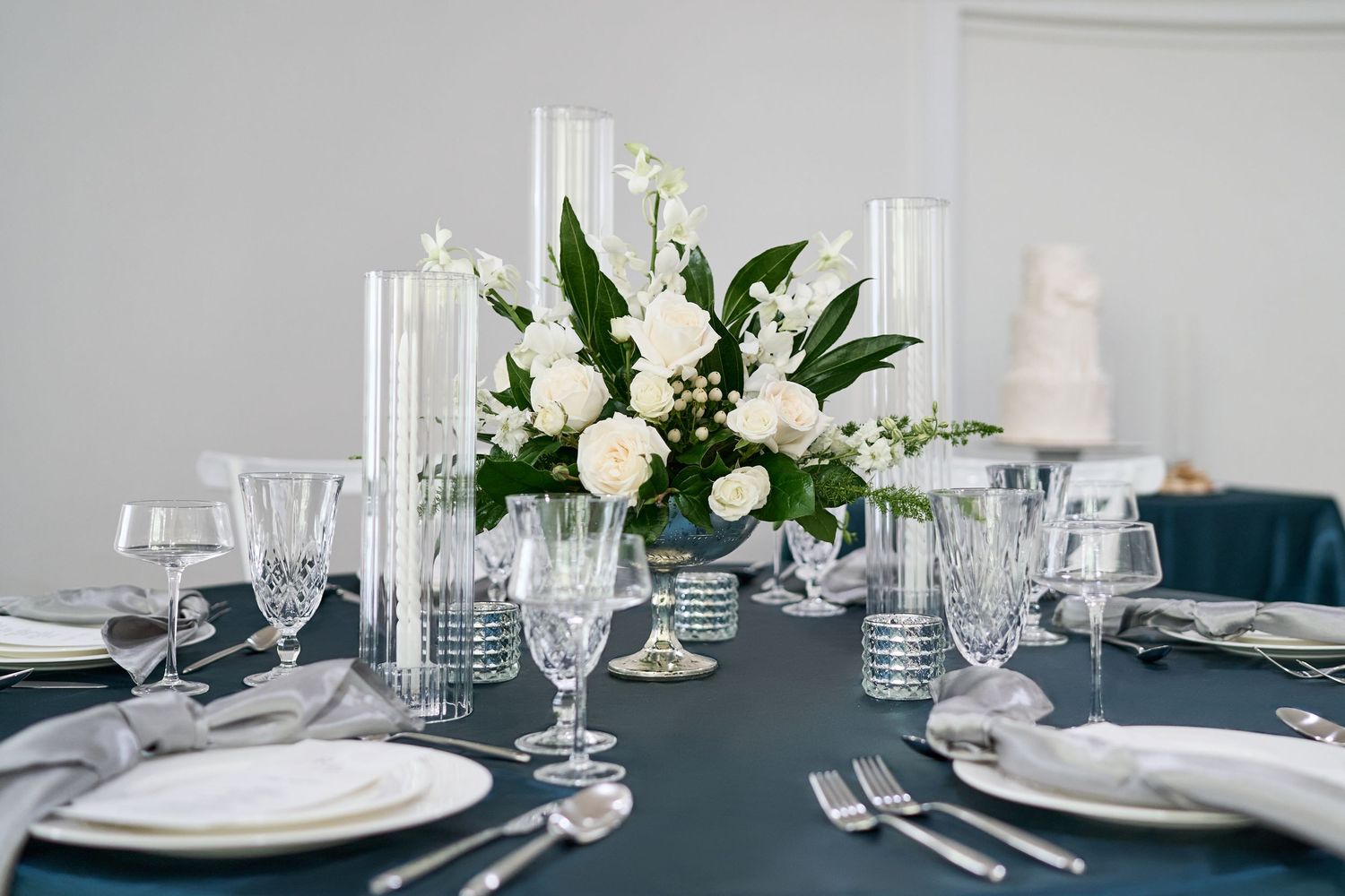 Elegant table setting with white floral centerpiece, crystal glasses and dark tablecloth.