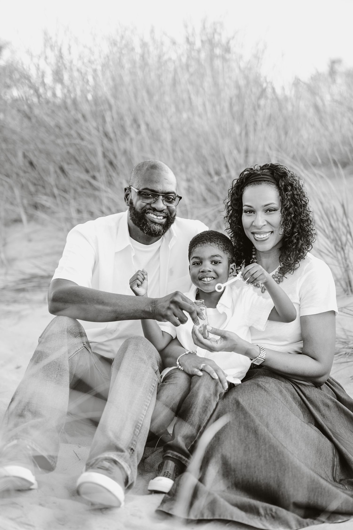 A couple sits together on sand dunes sharing playful and intimate moments in black and white photography.
