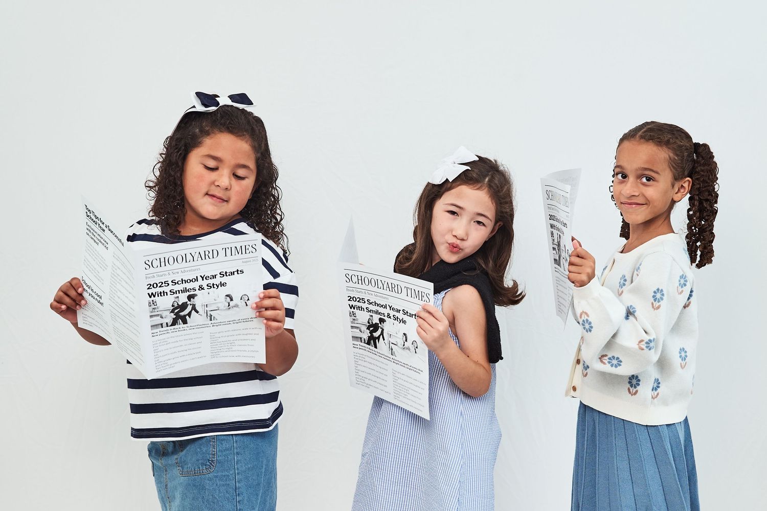 Three children in casual outfits reading newspapers together against a light background.