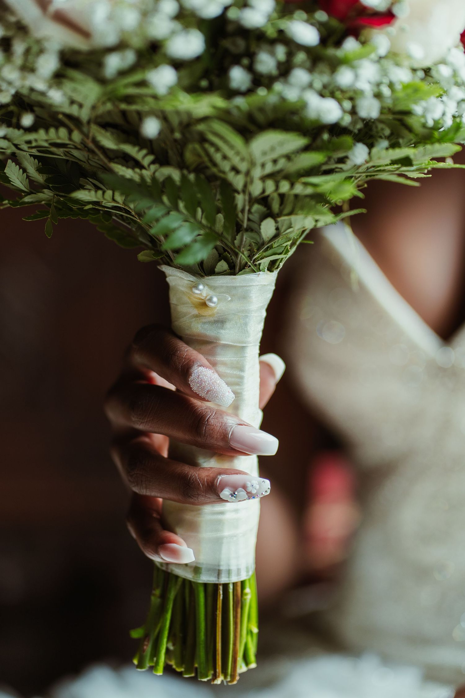 Wedding bouquet wrapped in white ribbon being held against a light background.