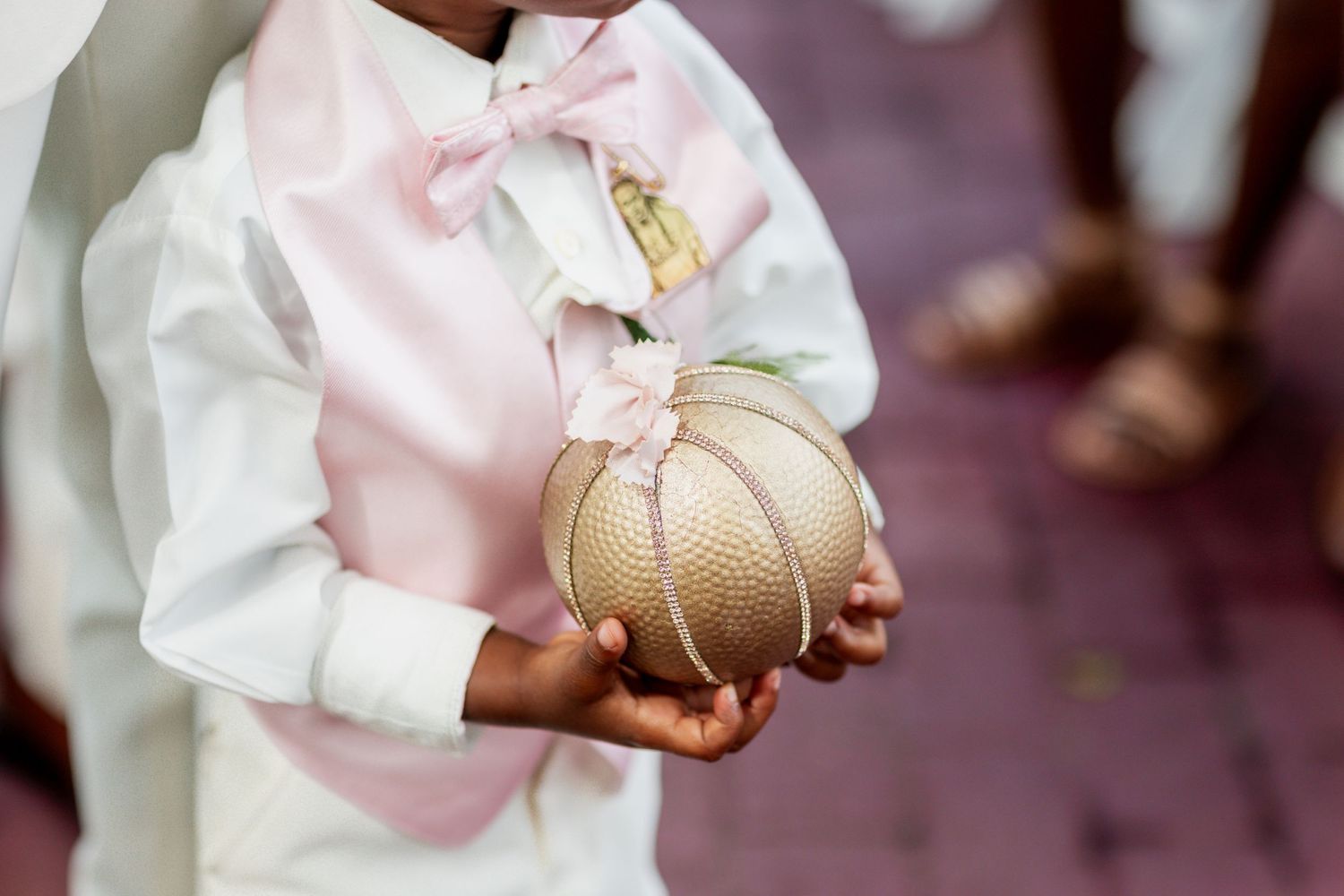 Hands holding a decorative gold sphere against pink and white formal attire.