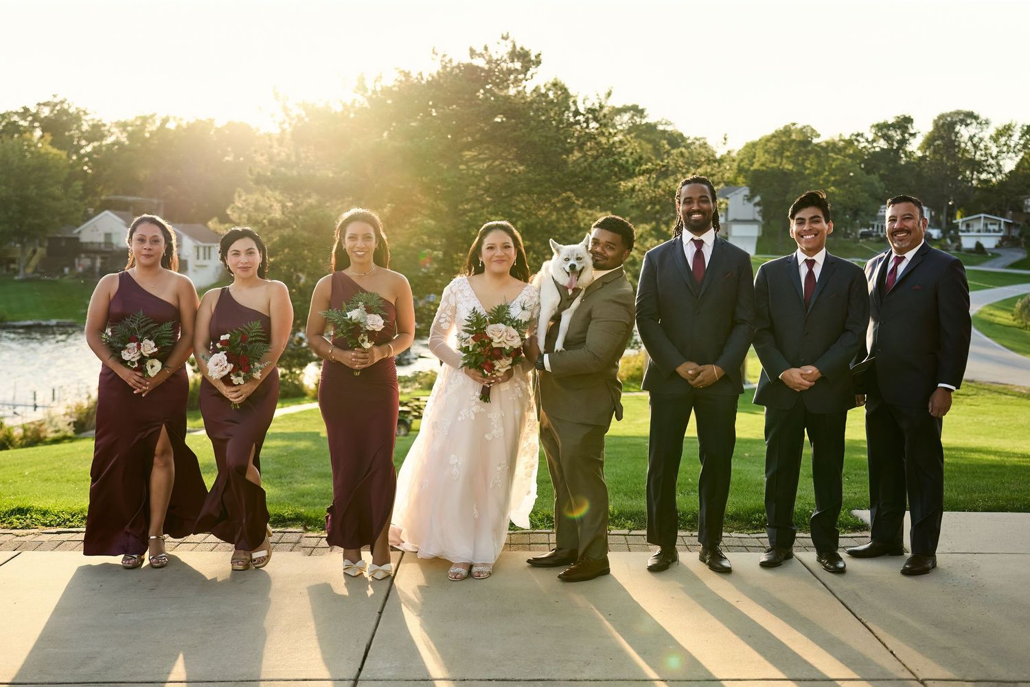 Wedding party poses together outdoors during golden hour sunset in a garden setting.