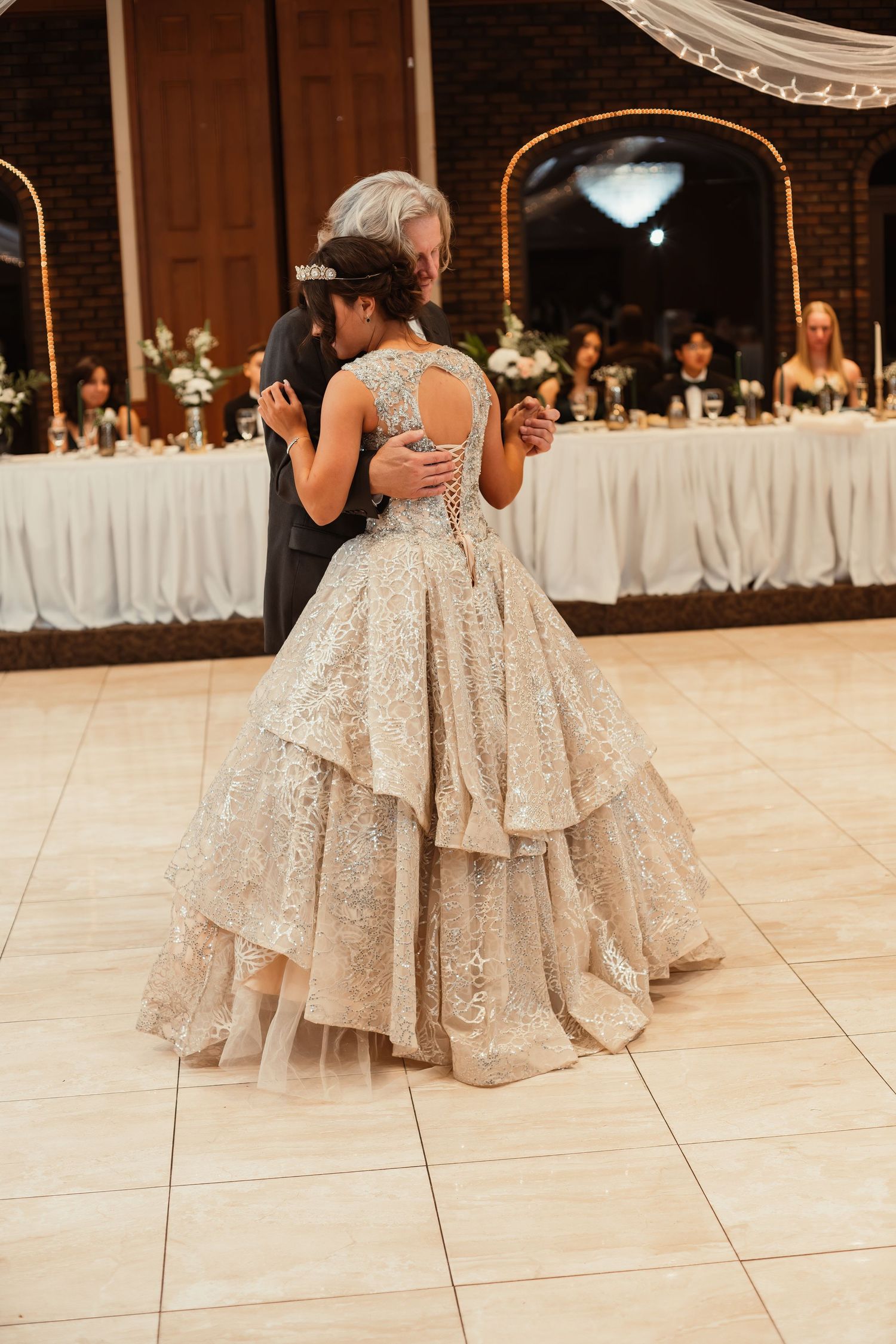 A wedding dance captured from behind, showcasing the bride's layered champagne ballgown on the dance floor.