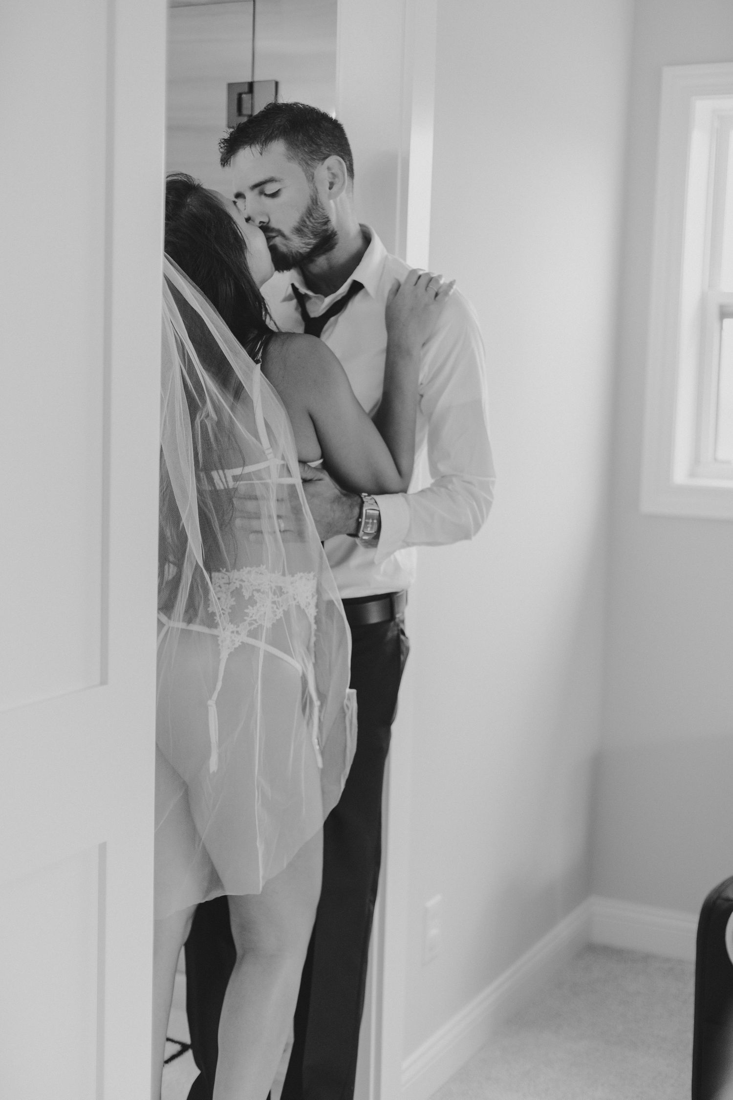 Black and white intimate portrait of couple in formal wear against white wall.