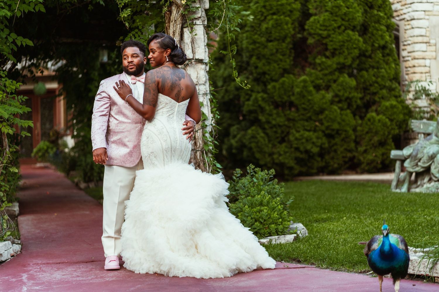 A wedding couple poses on red stairs with a peacock visible in the background.