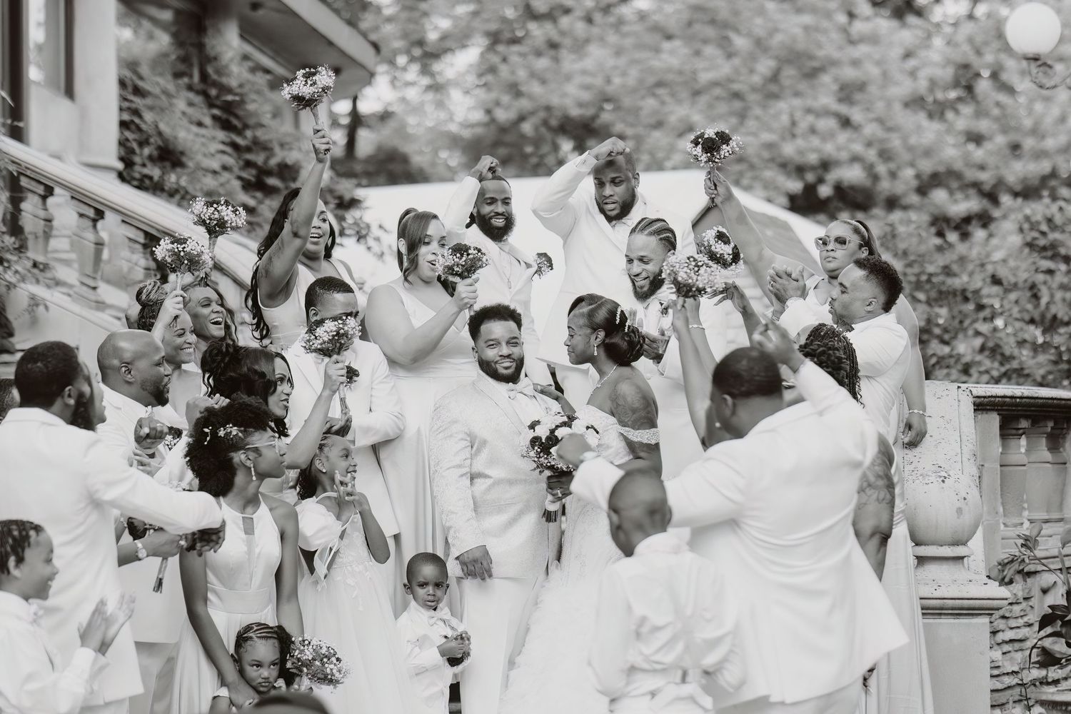 Black and white photo of joyful wedding party celebrating on outdoor stone steps.