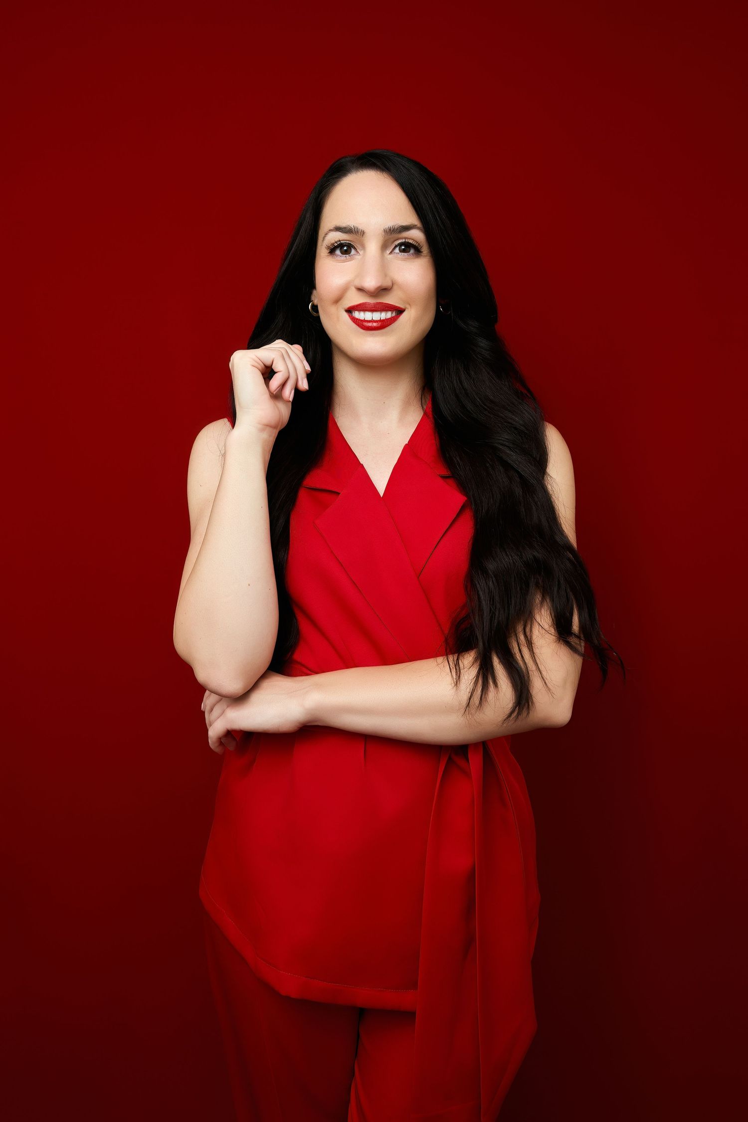 Long-haired woman in elegant red wrap dress poses confidently against a deep burgundy background.