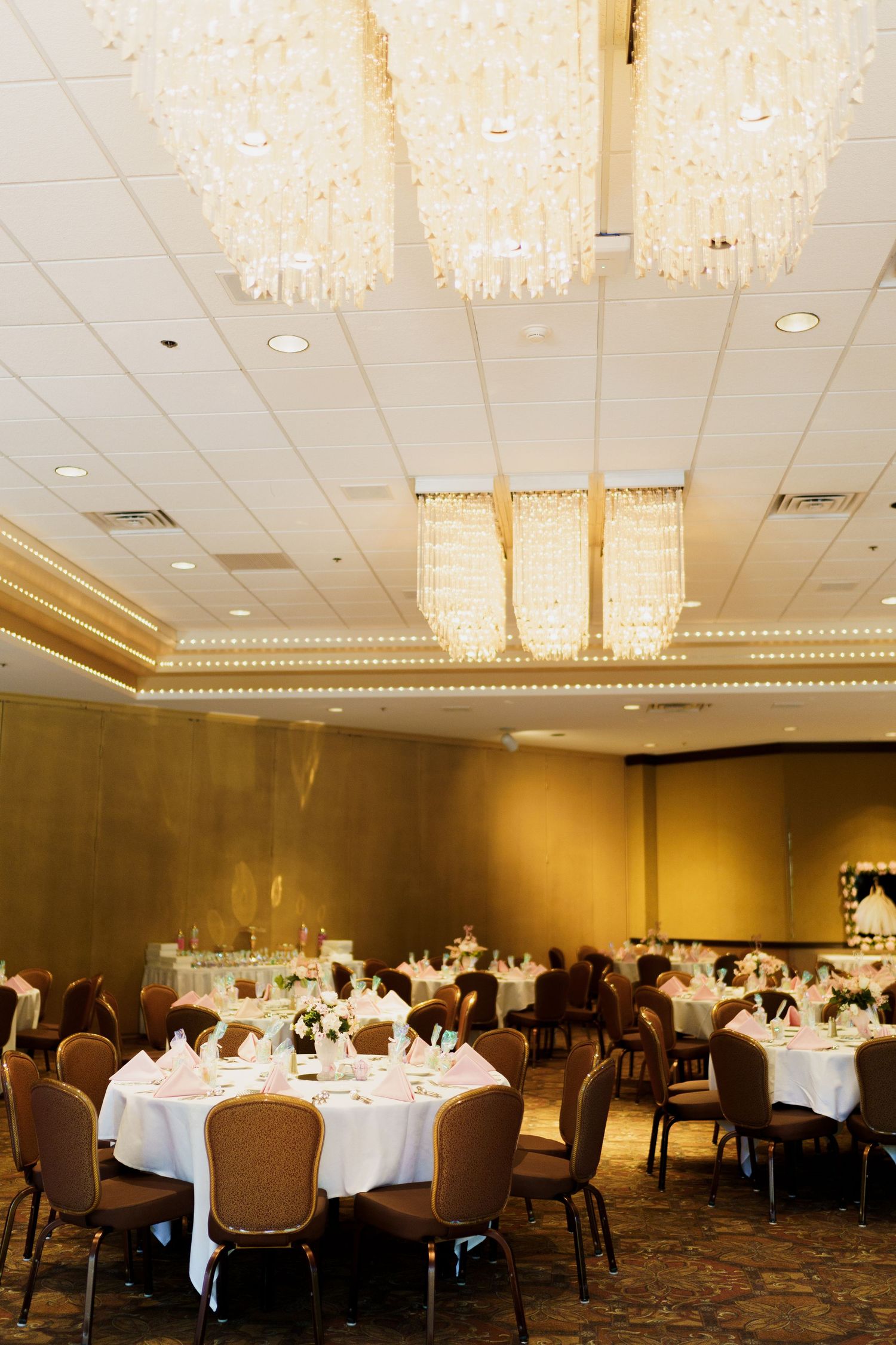 Elegant banquet hall with crystal chandeliers and round tables set with white linens for a formal event.