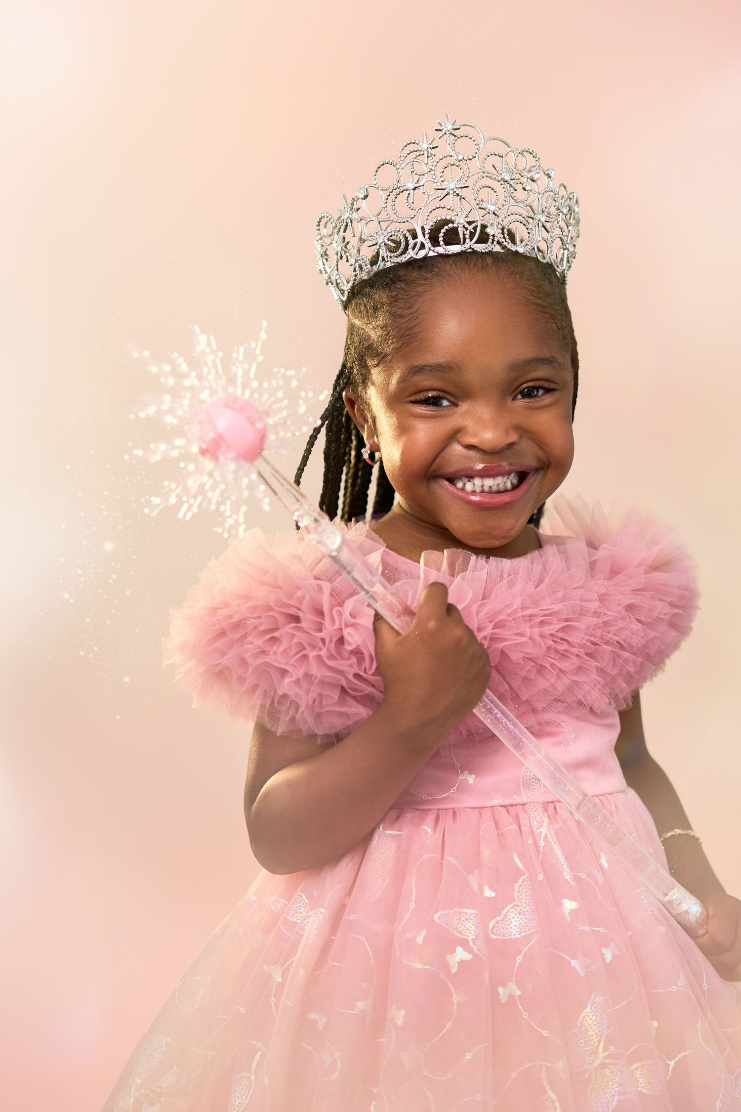 Young person wearing pink tulle dress and silver crown poses with smiles and joy in studio photos against pink backdrop.