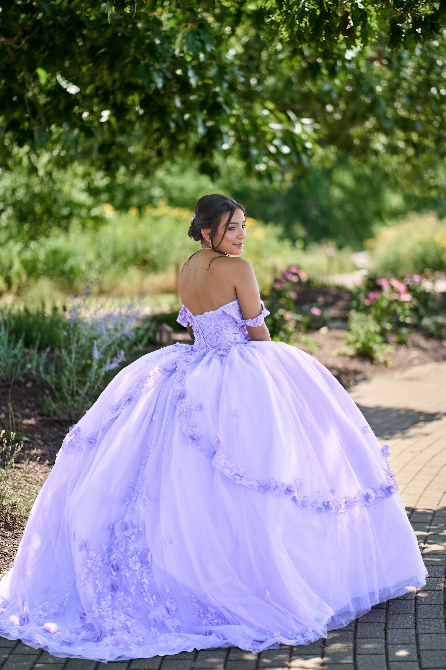 A stunning lavender quinceanera ball gown with off-shoulder design and floral appliques photographed in a garden setting.