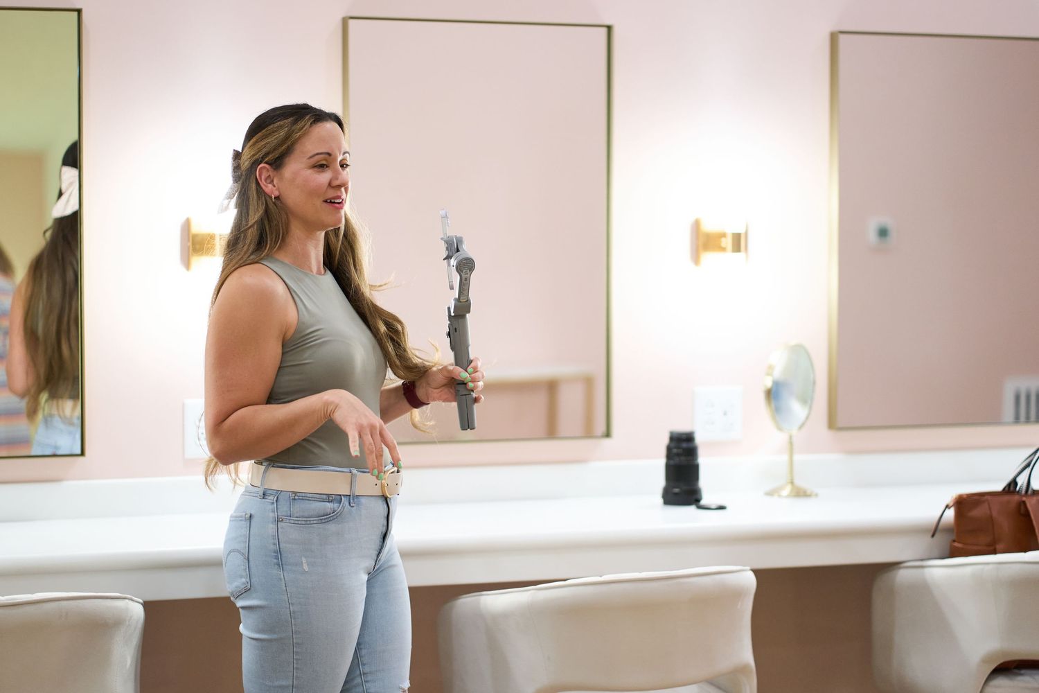 Woman in gray tank top stands at a makeup counter with mirrors and lights in a salon.