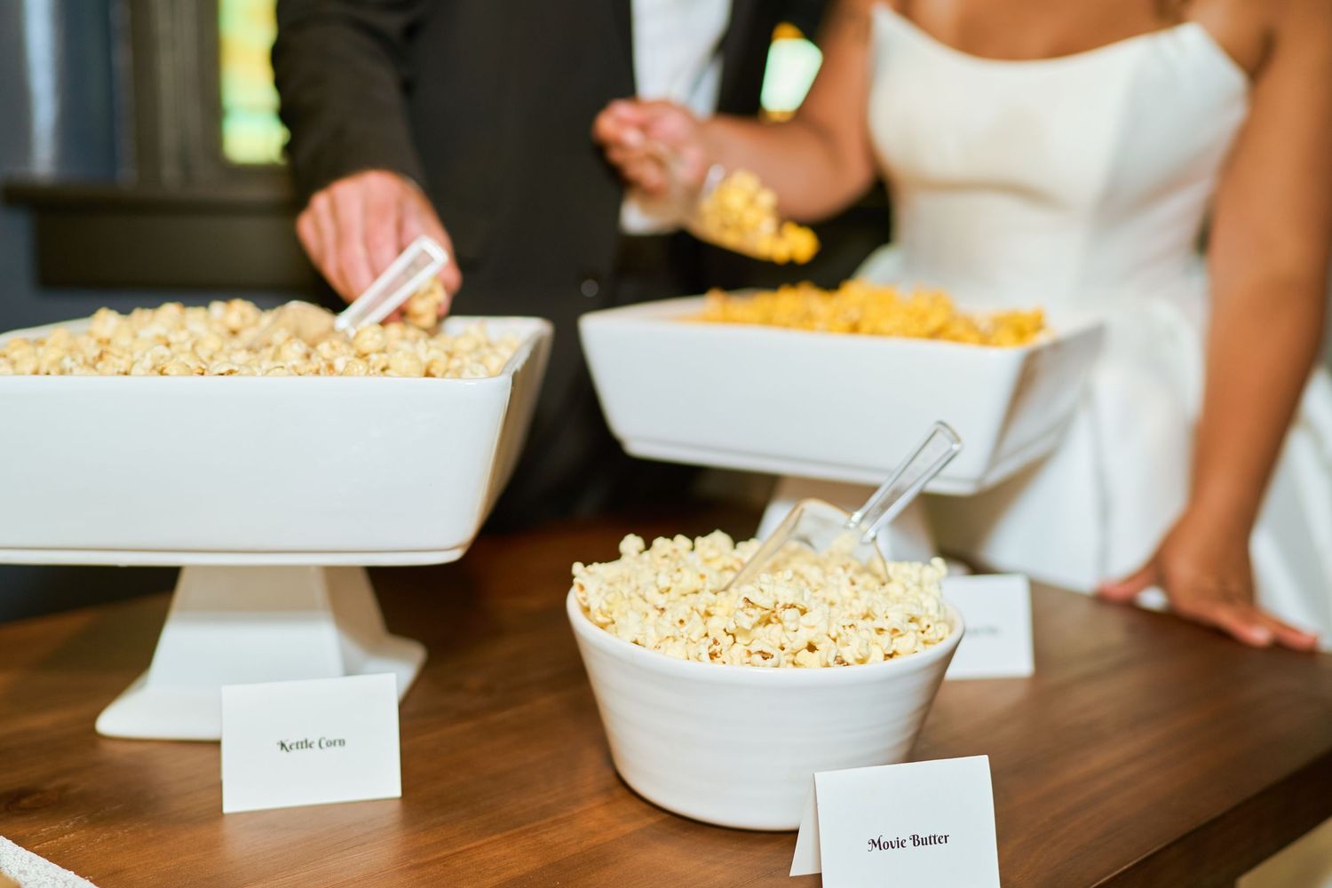 White serving bowls of snacks displayed on a dark wooden table at a wedding reception.