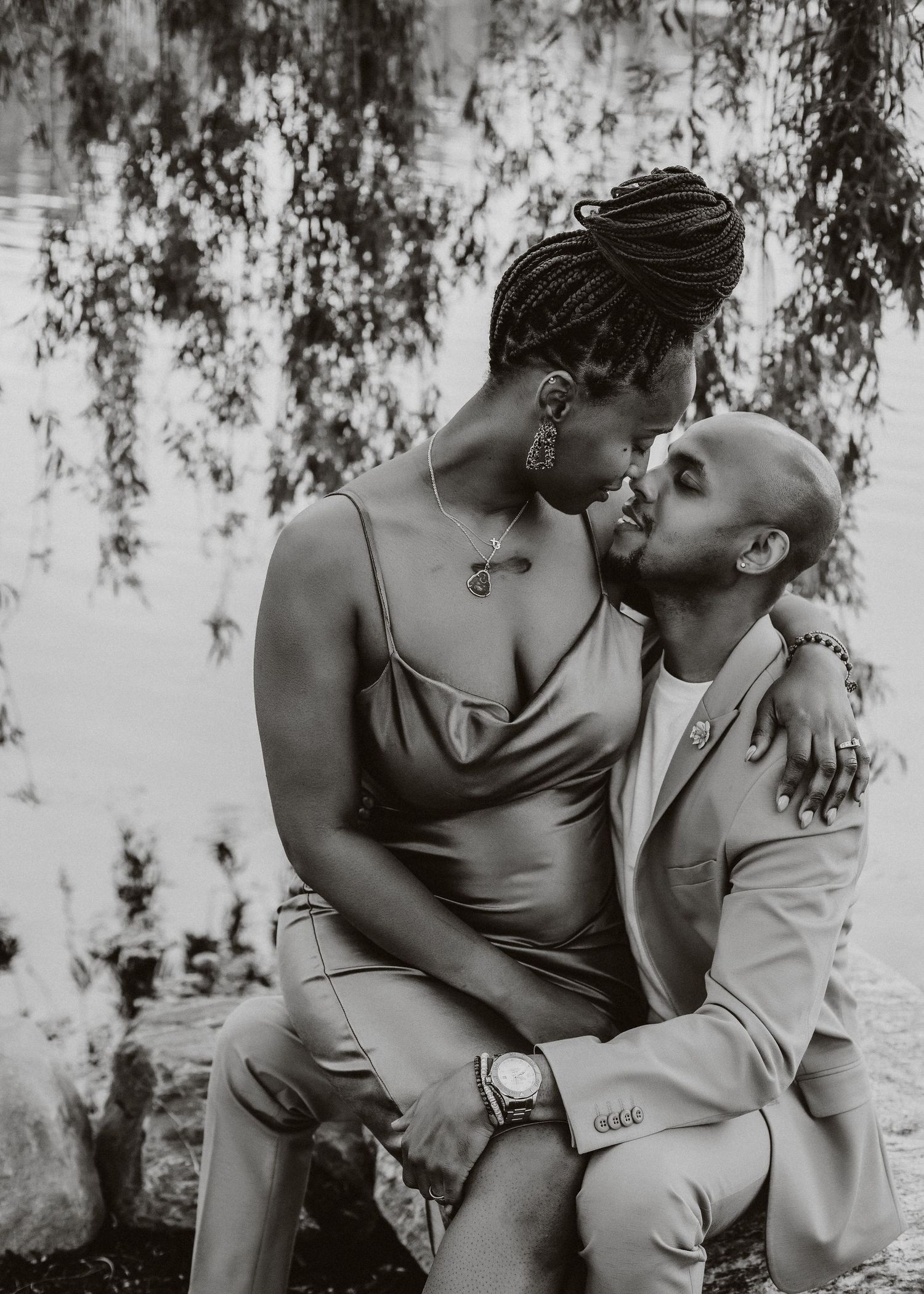 Intimate black and white portrait of couple embracing under willow tree branches.