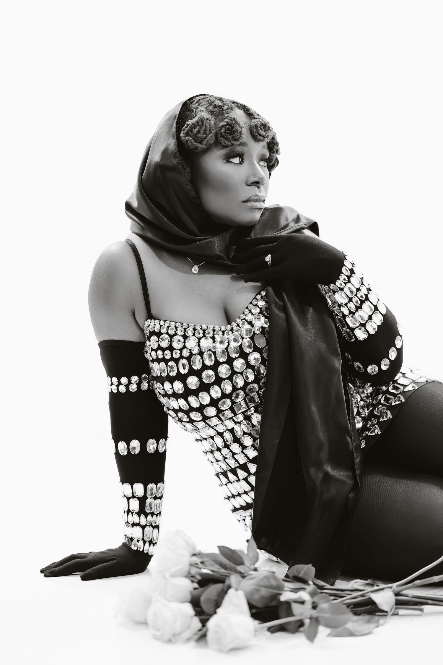 Black and white photo of model in crystal dress and headscarf posing with roses.