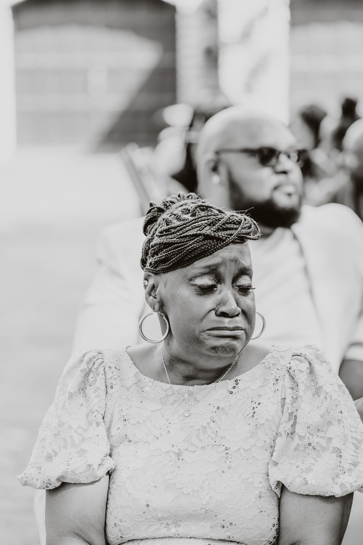 Wedding guest in elegant lace dress and headpiece shows emotional expression during ceremony.