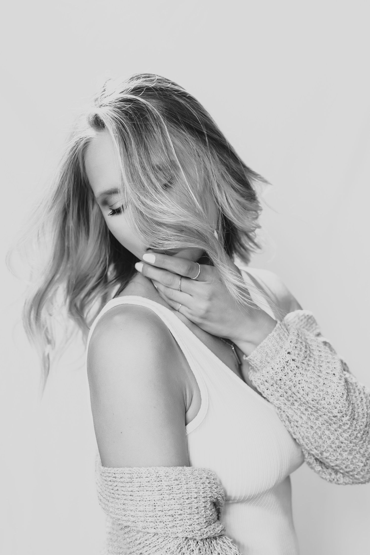 Black and white portrait photograph of someone in a knit sweater posing with eyes closed in soft natural lighting.