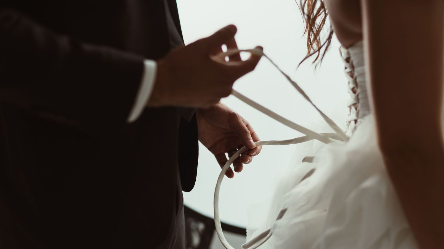 Silhouetted hands lacing up intricate wedding dress corset.