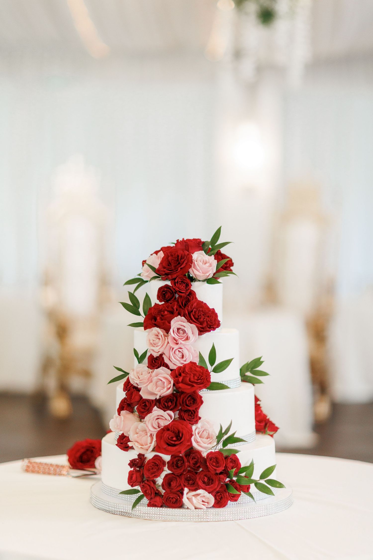 Three-tier white wedding cake decorated with cascading red and pink roses.