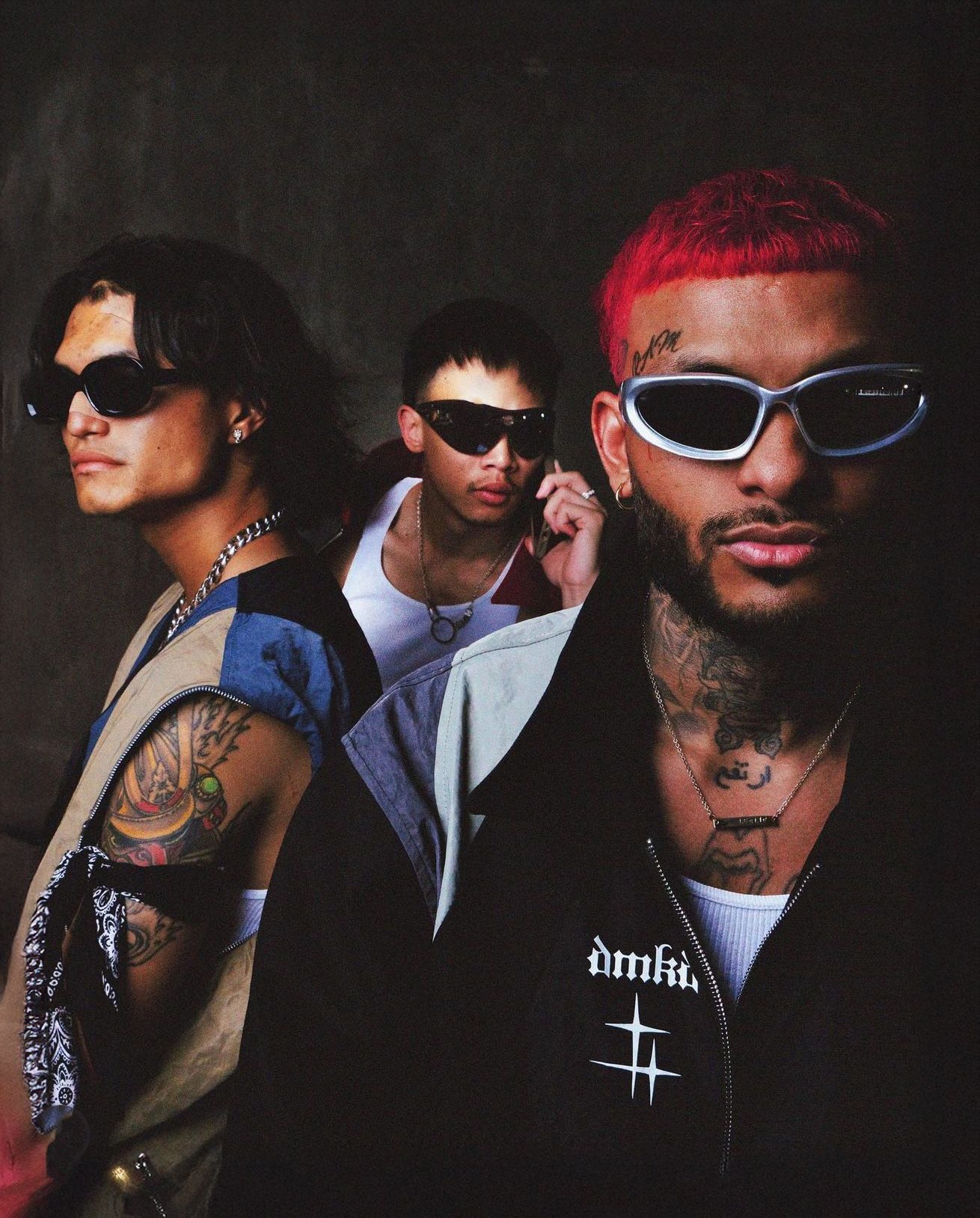 Group of people wearing sunglasses and dark clothing in dramatic lighting.