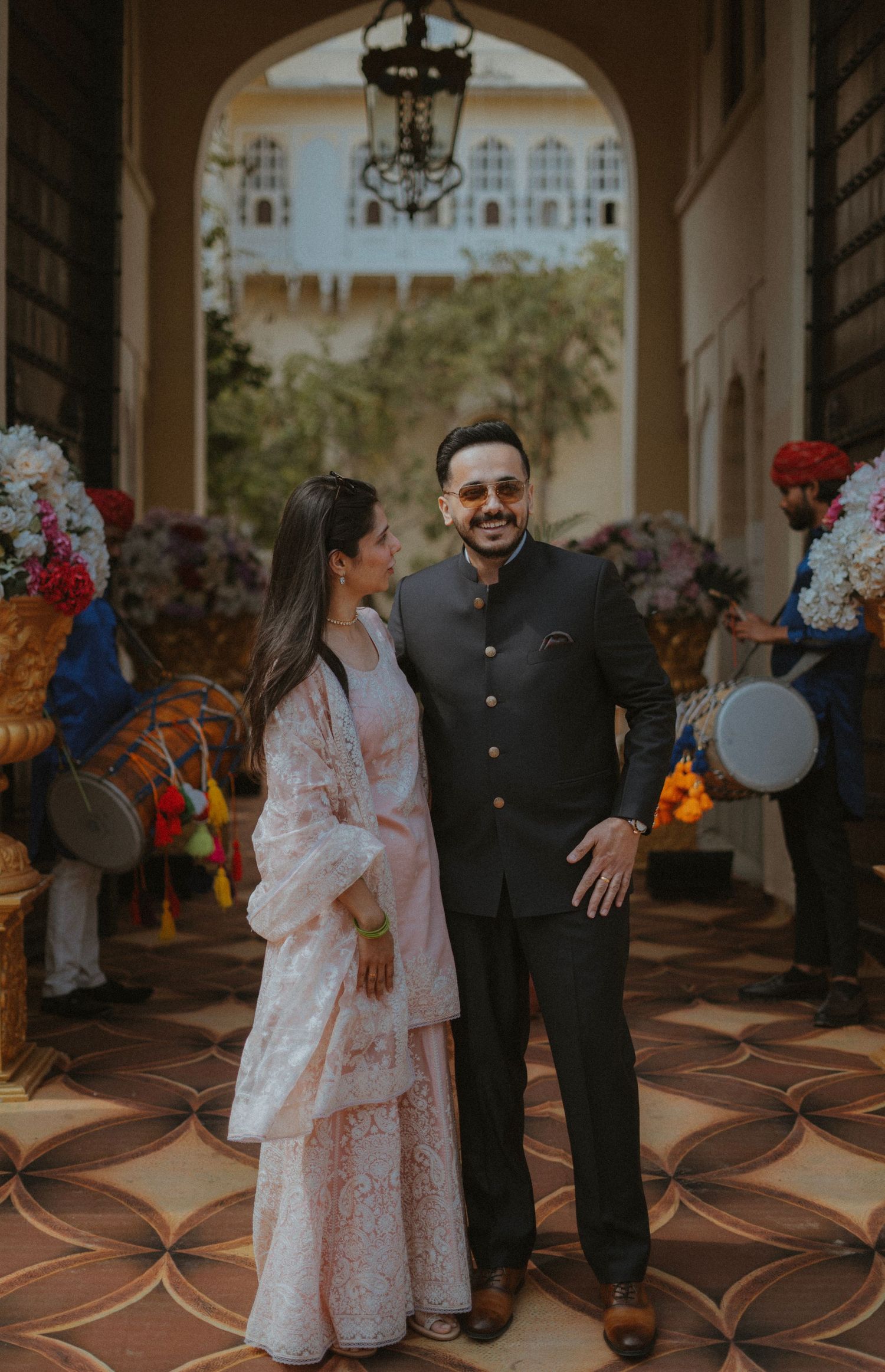 A couple shares a joyful moment in a grand hallway decorated with floral arrangements and ornate architectural details.