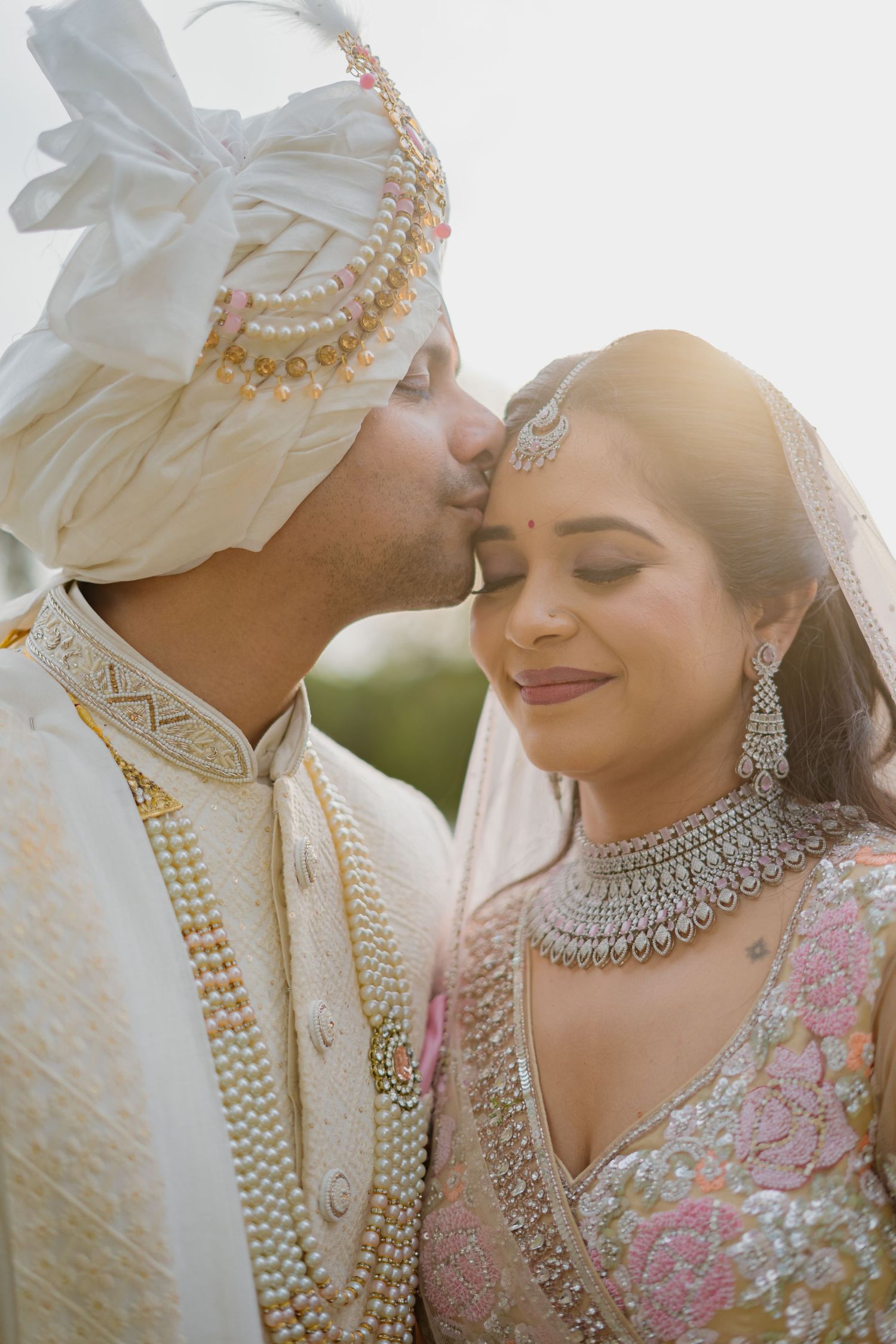 Romantic couple in traditional Indian wedding attire sharing an intimate moment in sunlight.
