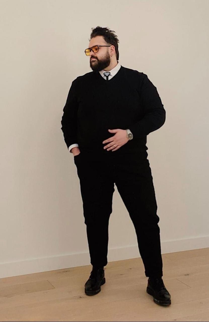 Person in black outfit sitting casually against light colored wall.