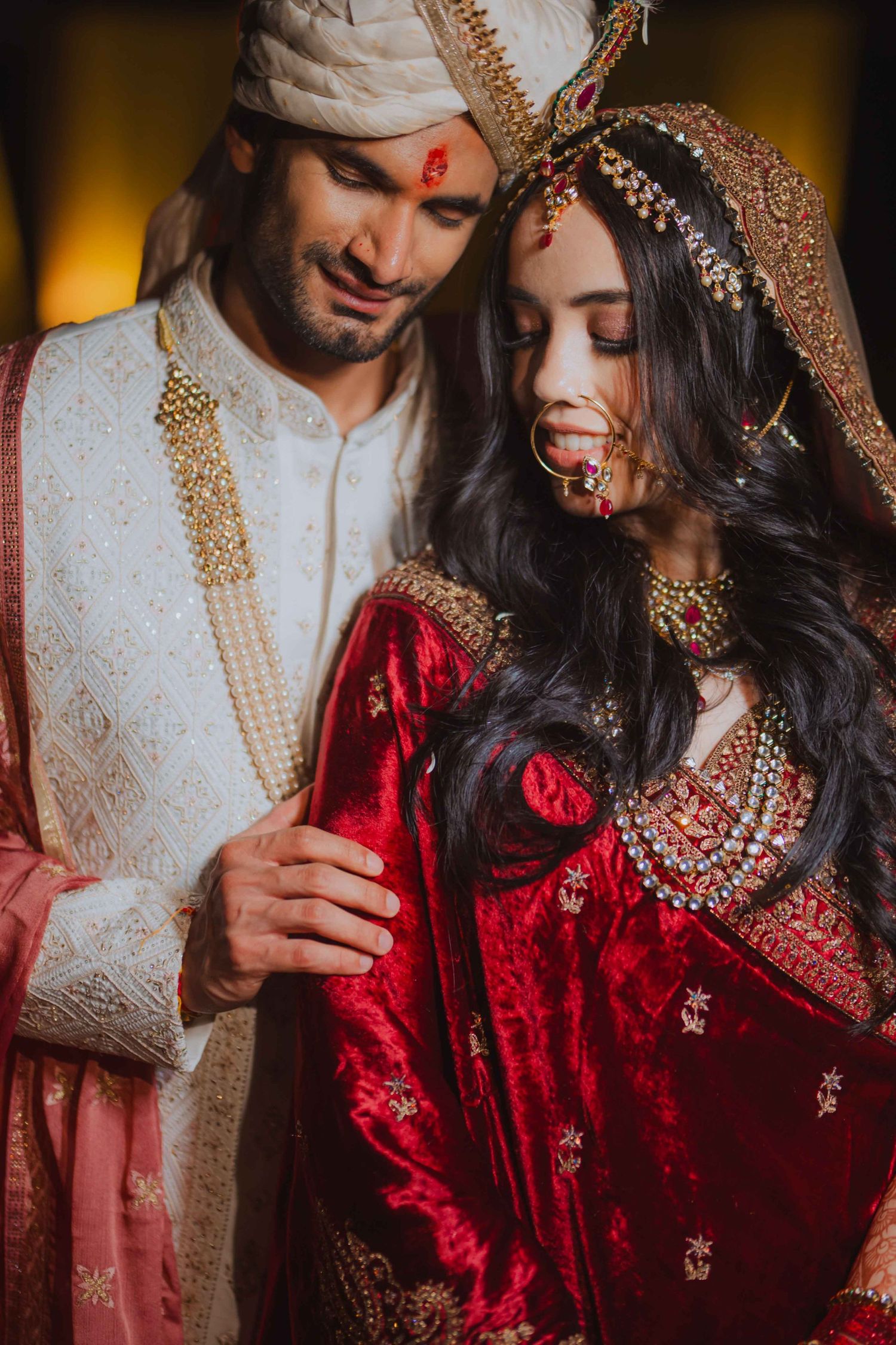 Elegant Indian wedding couple in traditional red and white wedding attire with ornate details.