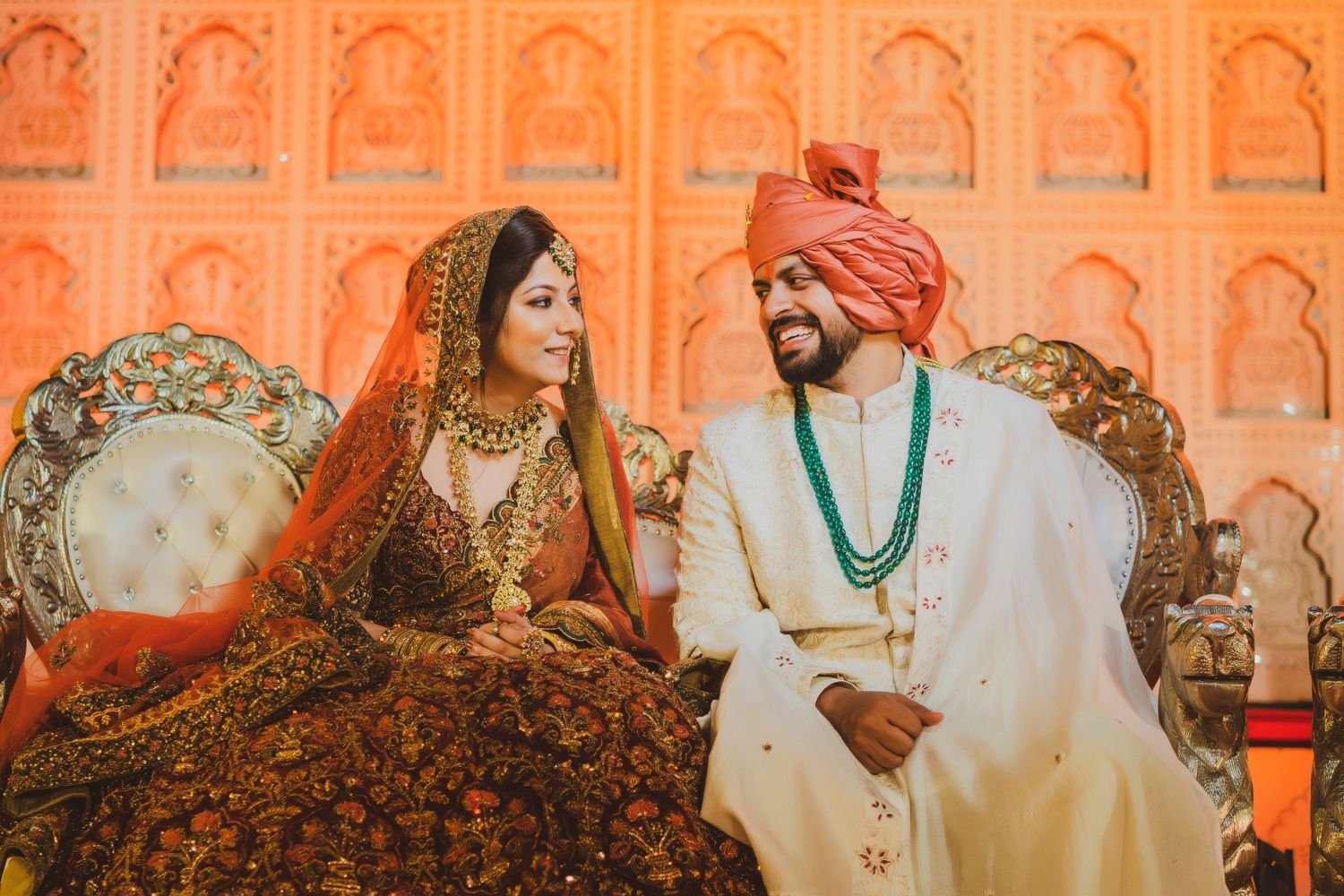 Traditional Indian wedding ceremony with orange decor and floral arrangements in the background.