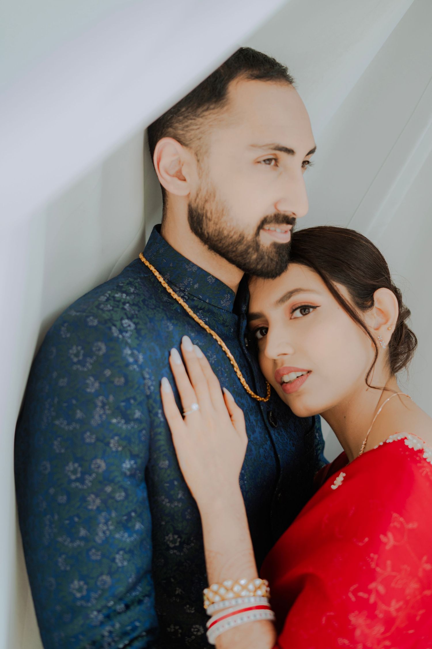 Intimate portrait of couple in navy and red traditional attire against white background.