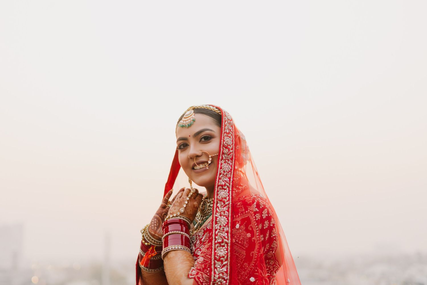 Bride in traditional red Indian wedding attire adorned with gold jewelry and embellishments.