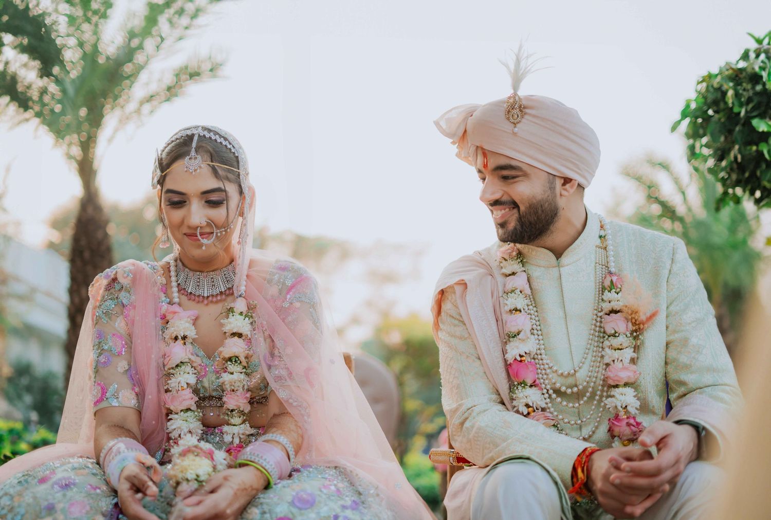 A couple in traditional South Asian wedding attire shares intimate moments during their outdoor ceremony celebration.