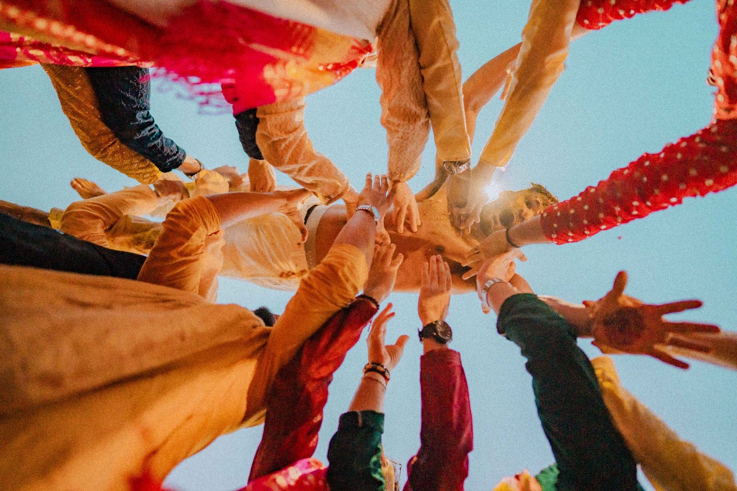 Low angle view of hands joining in a circle against blue sky with red decorations.