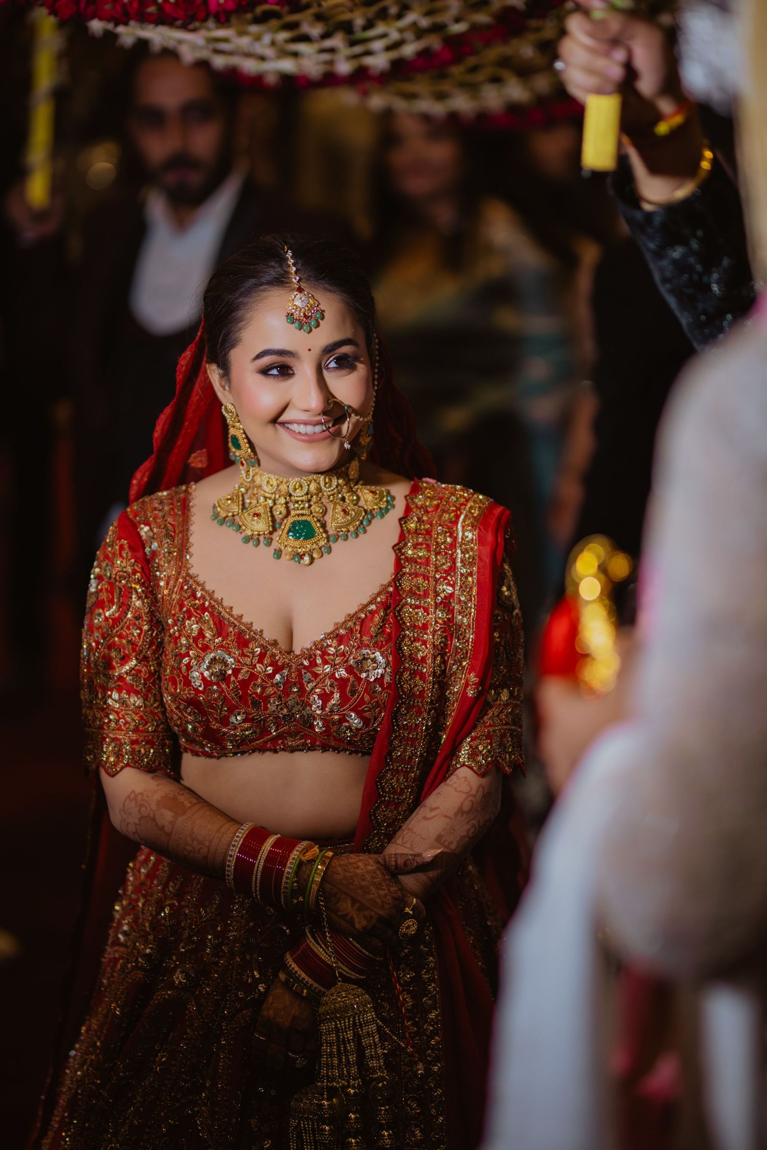 Bride in ornate red and gold traditional Indian wedding attire with stunning jewelry.