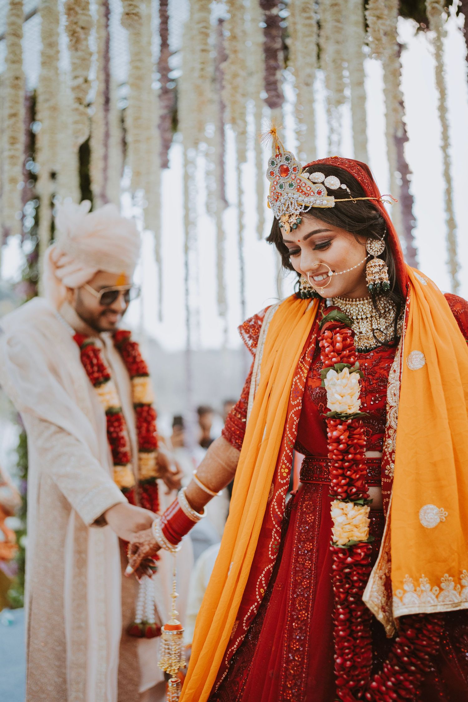 Wedding ceremony setup with hanging floral decorations and couple in traditional Indian attire.