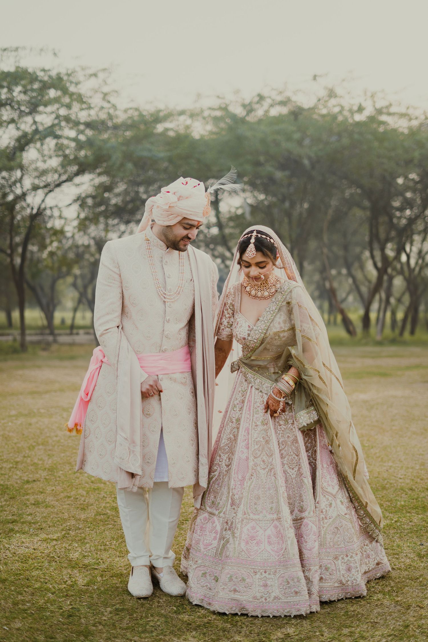 Couple in traditional Indian wedding attire walking together through a scenic park.