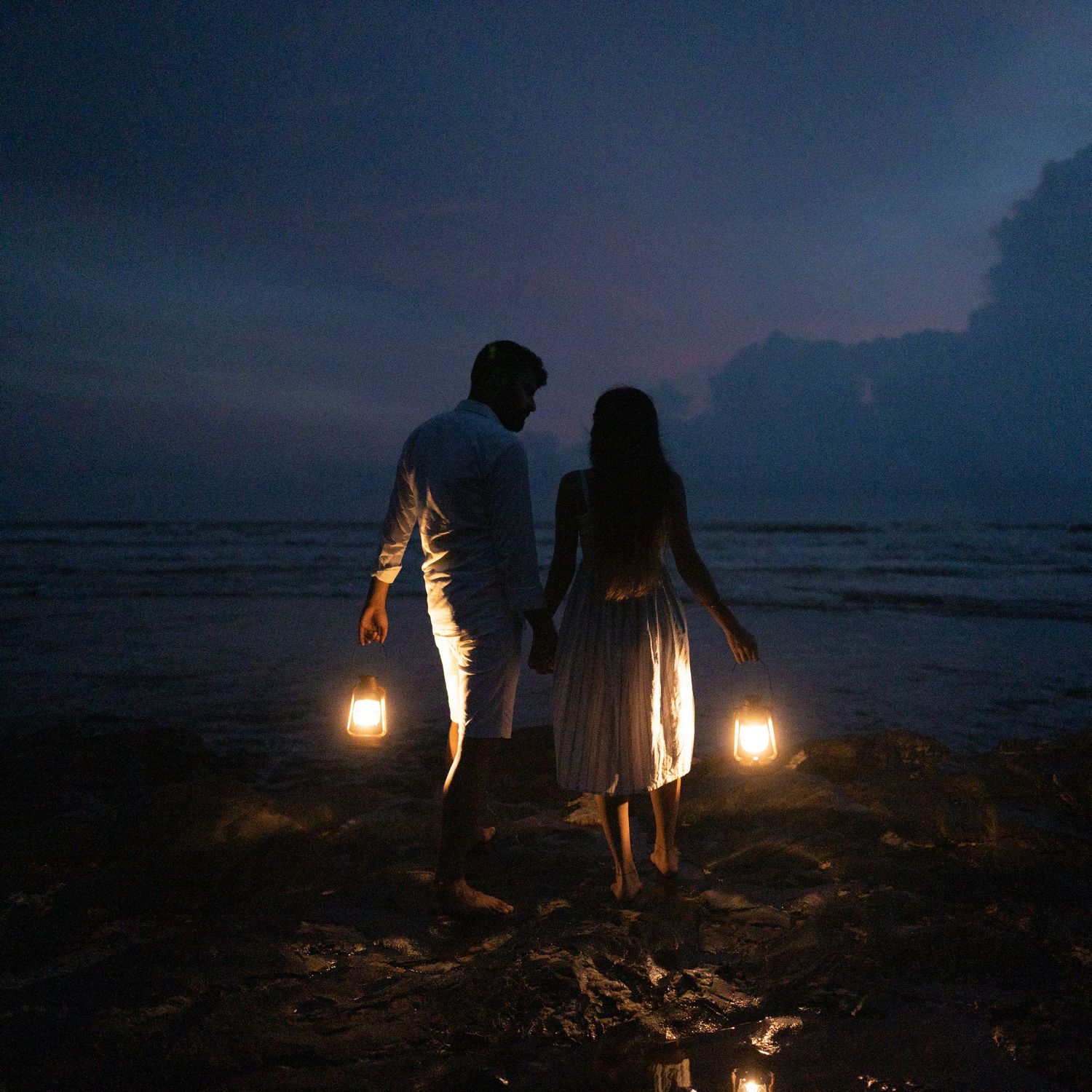 Group holding lanterns on a dark beach at sunset with moody dramatic sky in the background.