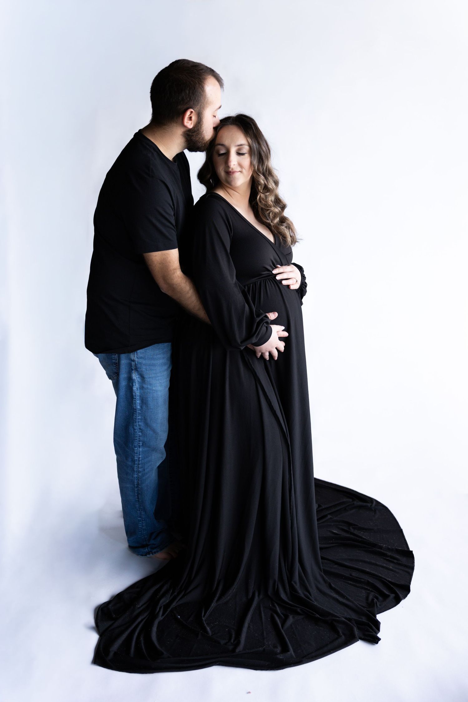 Couple in black attire embraces intimately in minimalist white studio setting across multiple artistic poses.