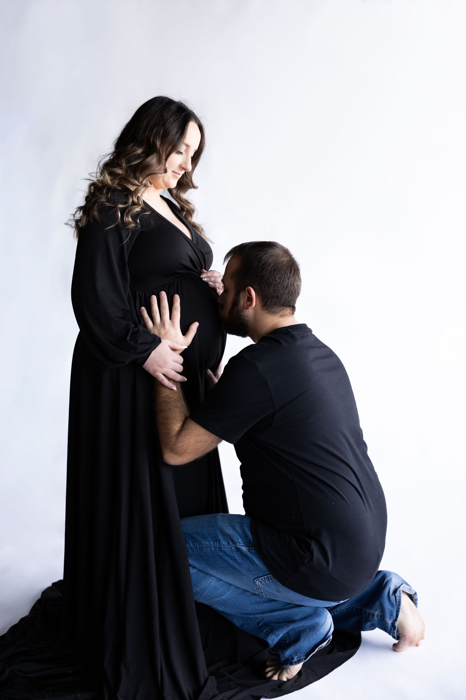 Dramatic black and white maternity portrait with flowing dress against light background.