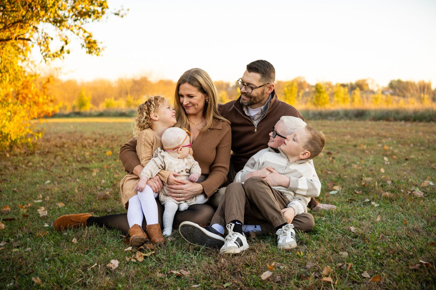 A family enjoys quality time together on grass during golden hour autumn sunset in a park setting.