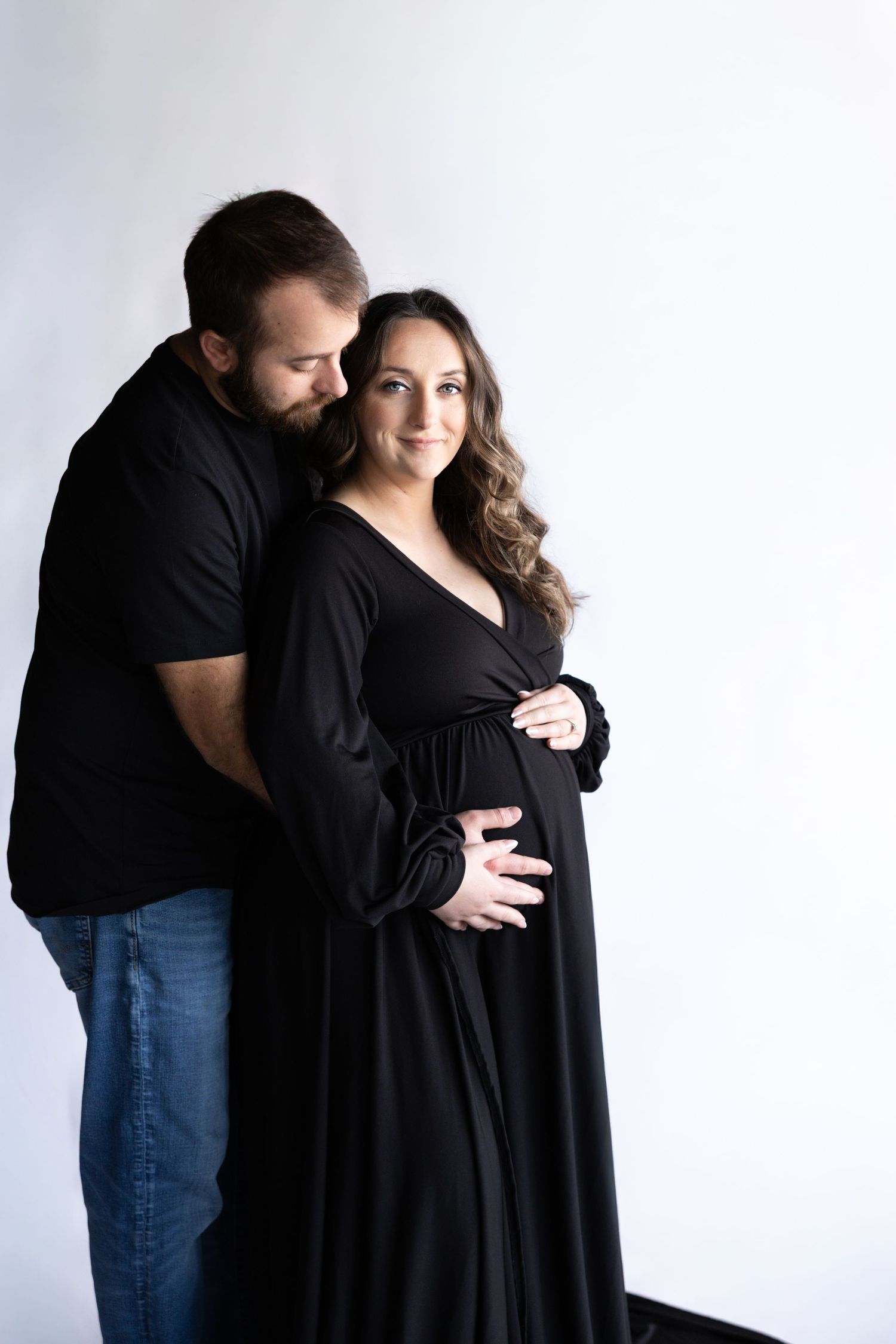Intimate maternity portrait against white backdrop featuring a couple in matching black outfits.