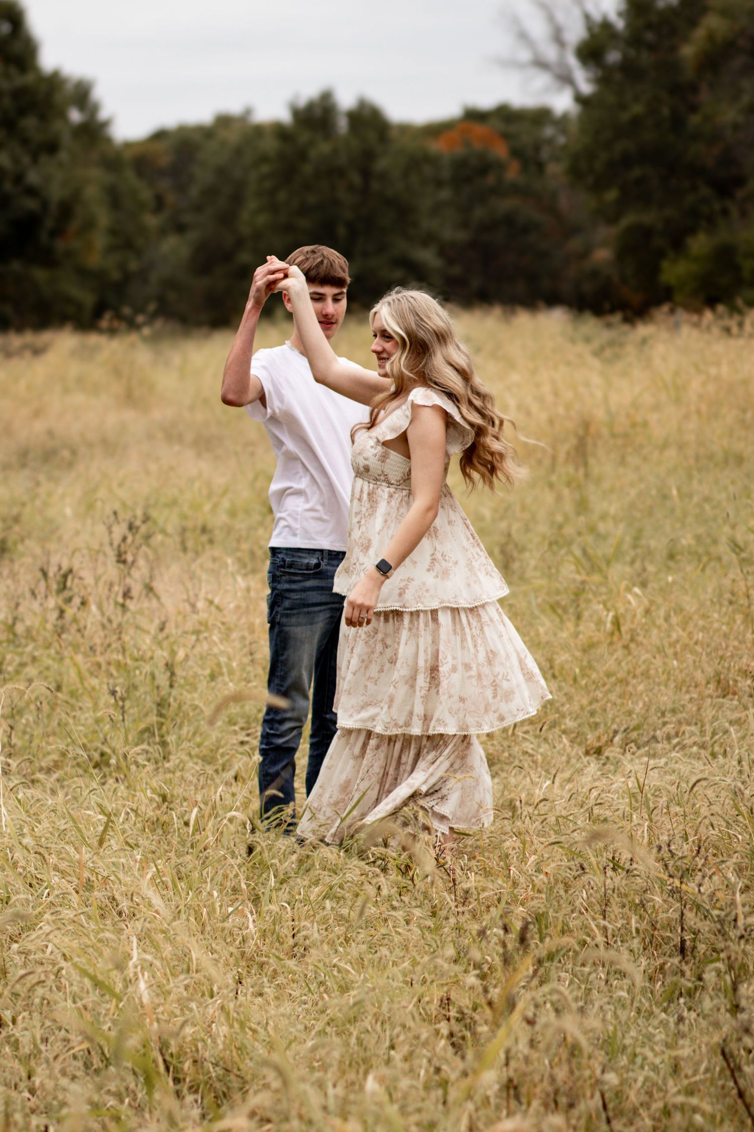 A couple dances together in a golden meadow during sunset, twirling and embracing in a romantic moment.