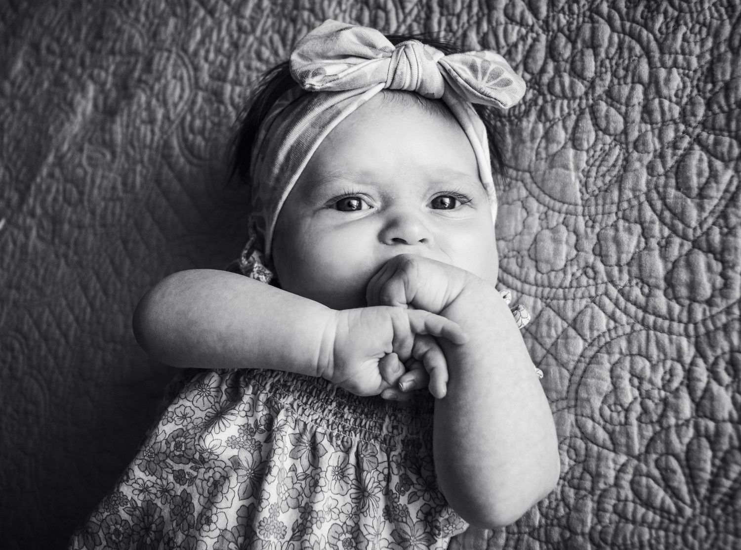 Black and white series of a baby showing playful expressions while lying on a quilted surface.