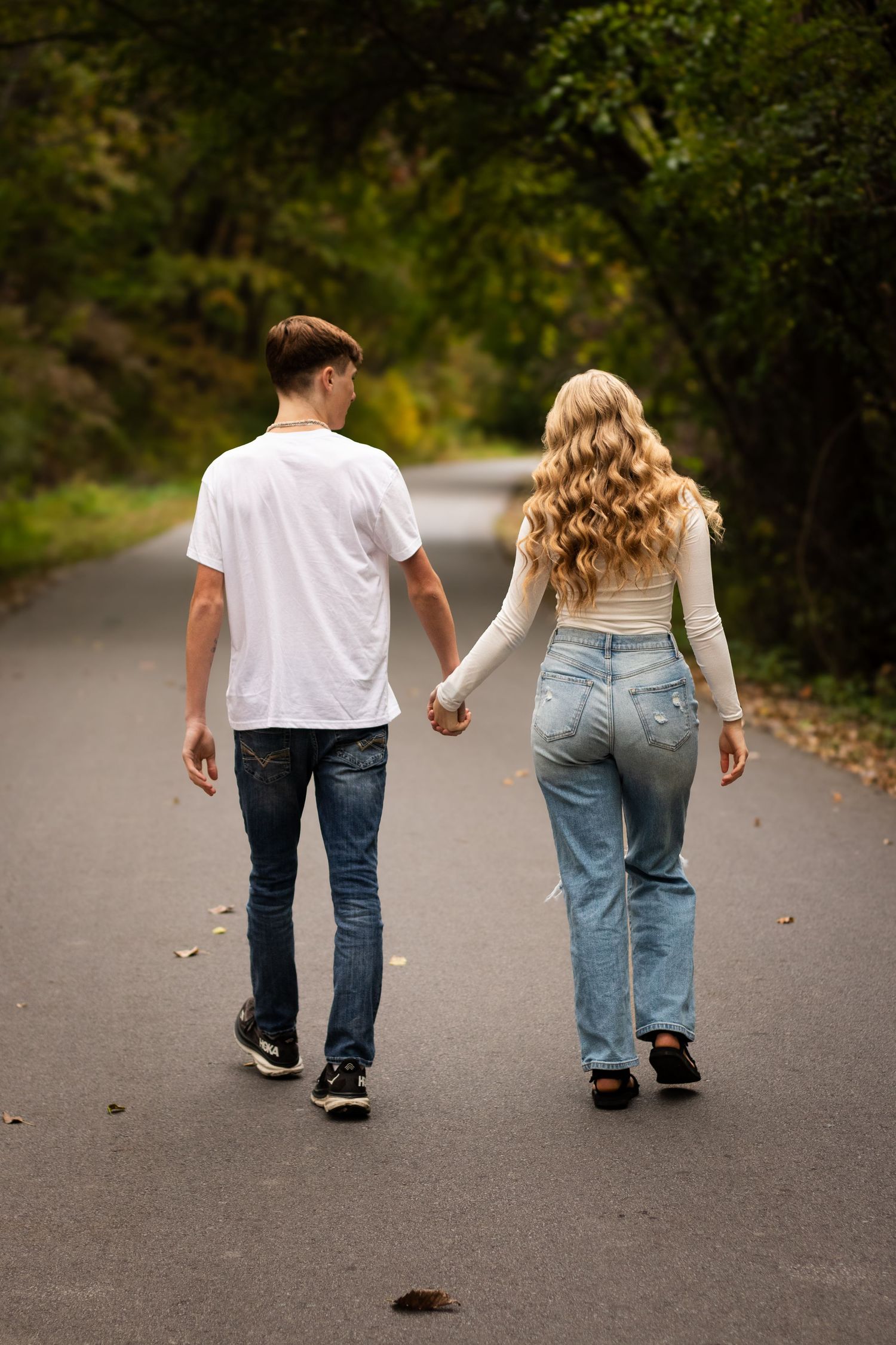 A couple walking together on a paved path through autumn trees, shown in a sequence of five connected photos.