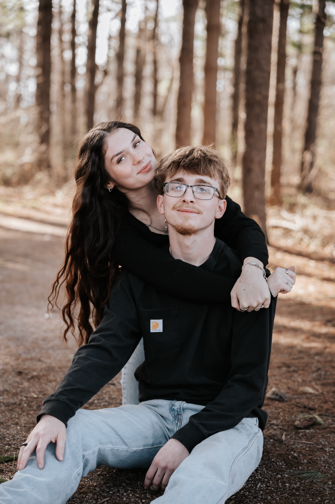 A couple in black sweaters sharing an intimate moment while sitting on a forest path during autumn.