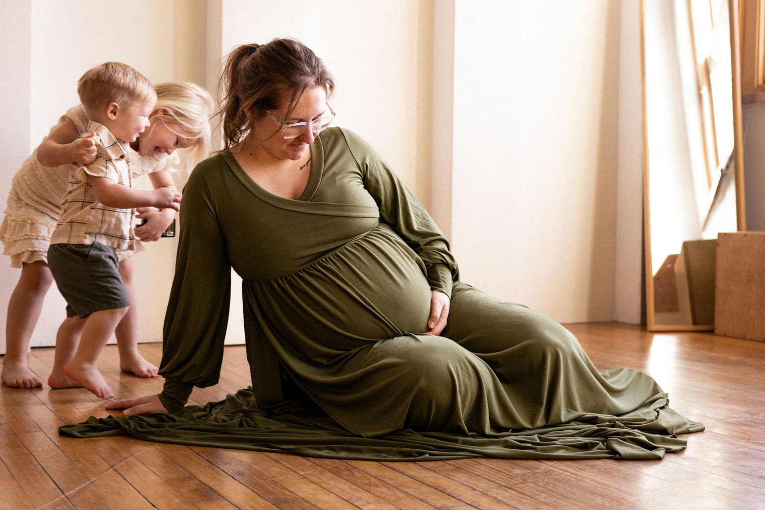 A person in an olive green dress lies on the floor with a baby in a series of tender candid moments.