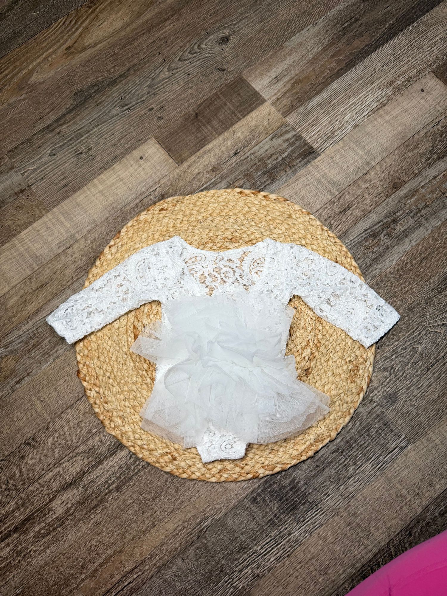 White lace long-sleeve baby romper with tutu skirt displayed on woven mat on wood floor.