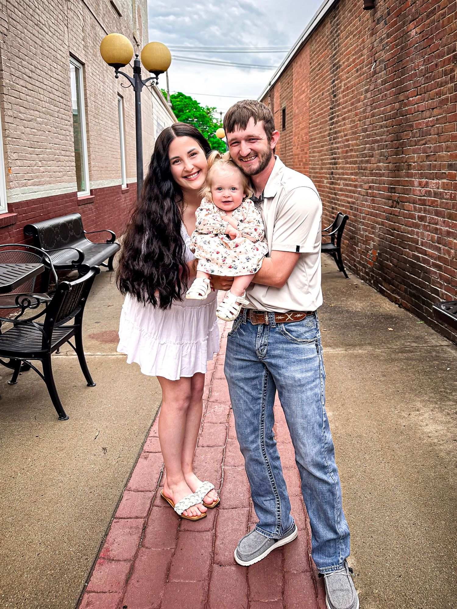A family in coordinating pink and denim outfits poses together in a brick-lined alleyway.